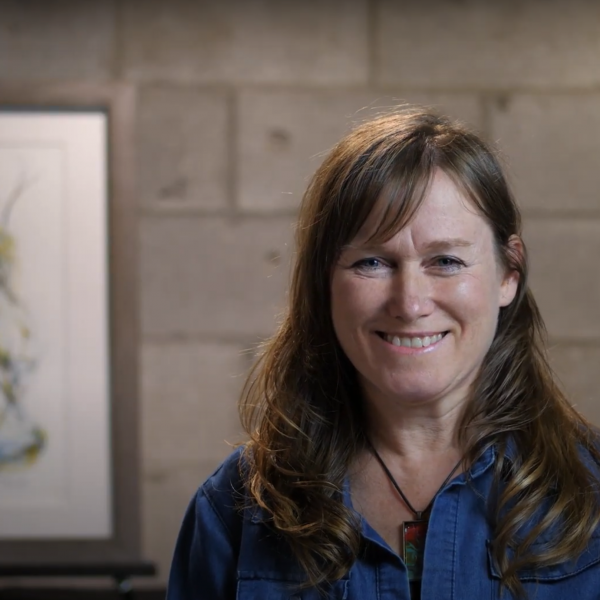 A photo of artist Catherine Luce smiling in front of her painting.
