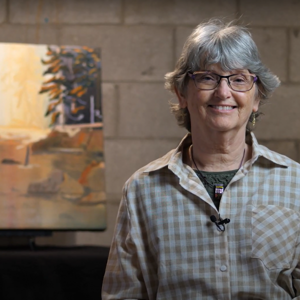 A photo of artist Pam Mackenzie smiling in front of her painting.